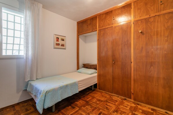Une chambre avec un lit simple, une armoire en bois, une fenêtre avec des rideaux et une petite table de chevet.