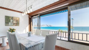 A dining area with a table set for four, large windows with a view of the sea, and a painting on the wall.