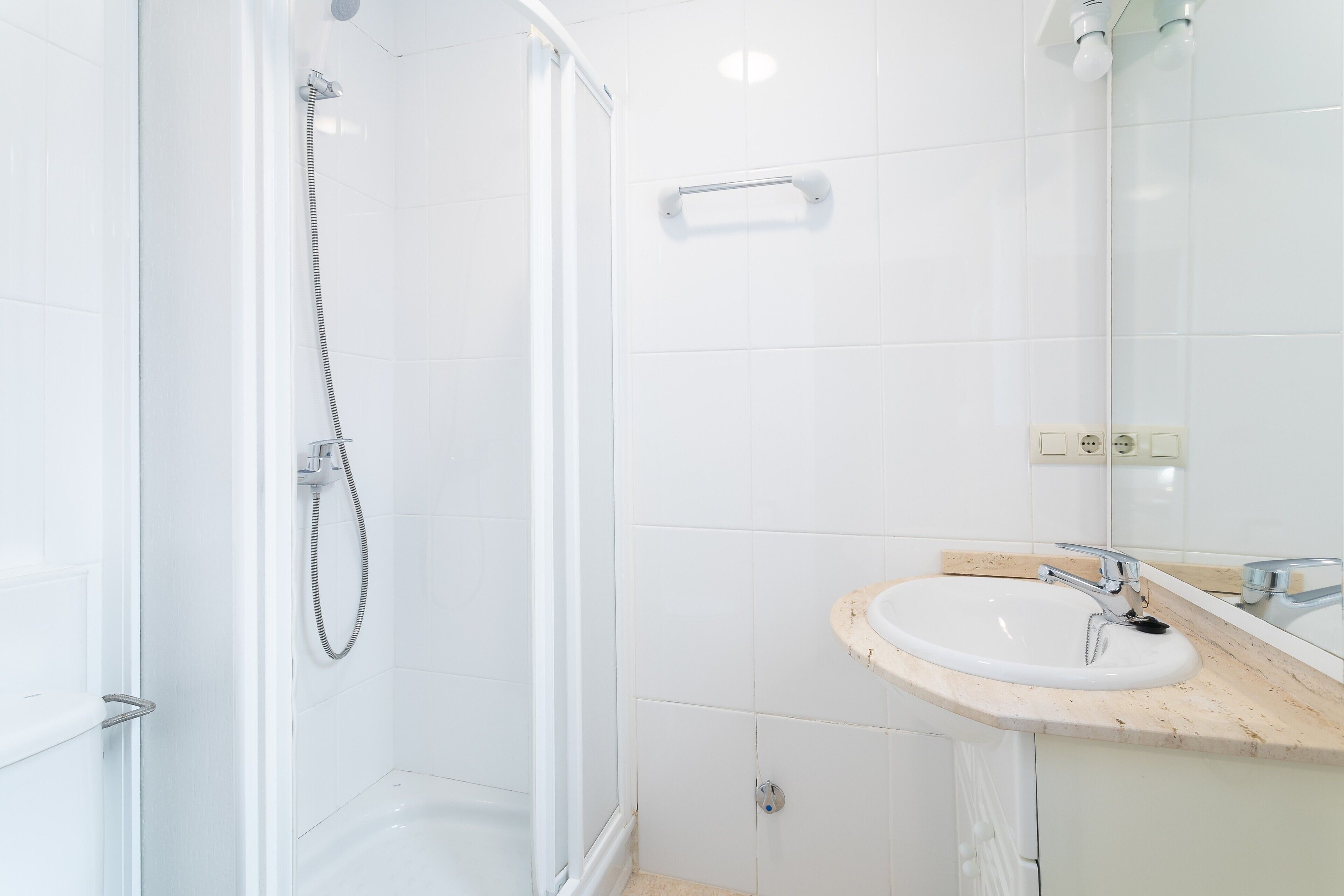 Une salle de bain avec une douche à parois de verre, un lavabo avec un miroir et des murs recouverts de carreaux blancs.