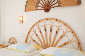 Een bed met een bamboe hoofdbord, een ventilator aan de muur en een nachtkastje met een lamp.