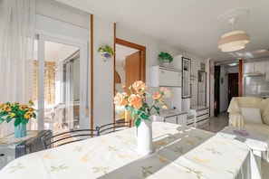Een eetgedeelte met een tafel voor twee personen, een vaas met bloemen en uitzicht door een glazen deur.