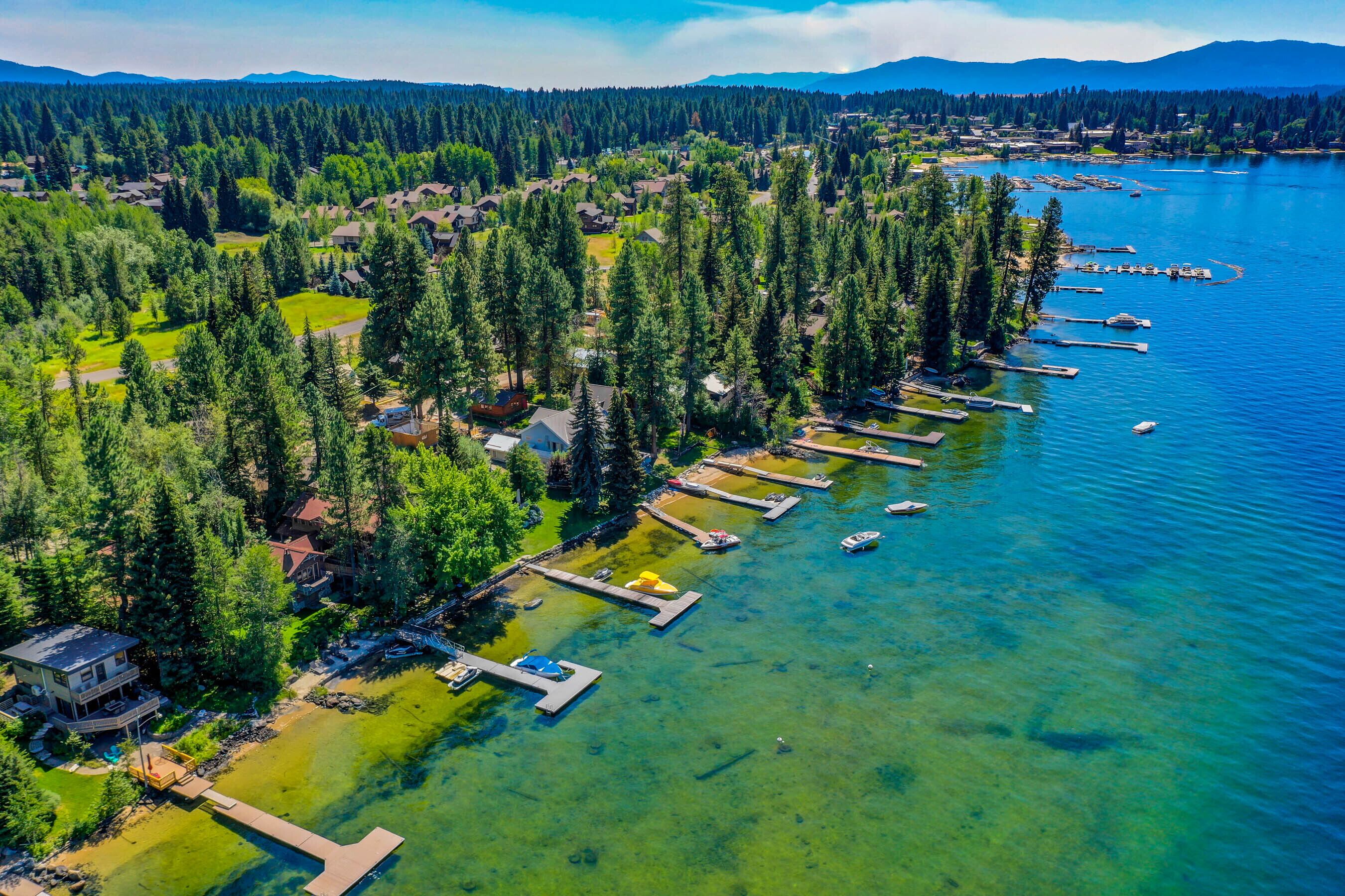An aerial view of a lakeside property with multiple docks and boats, surrounded by dense forest and residential buildings.