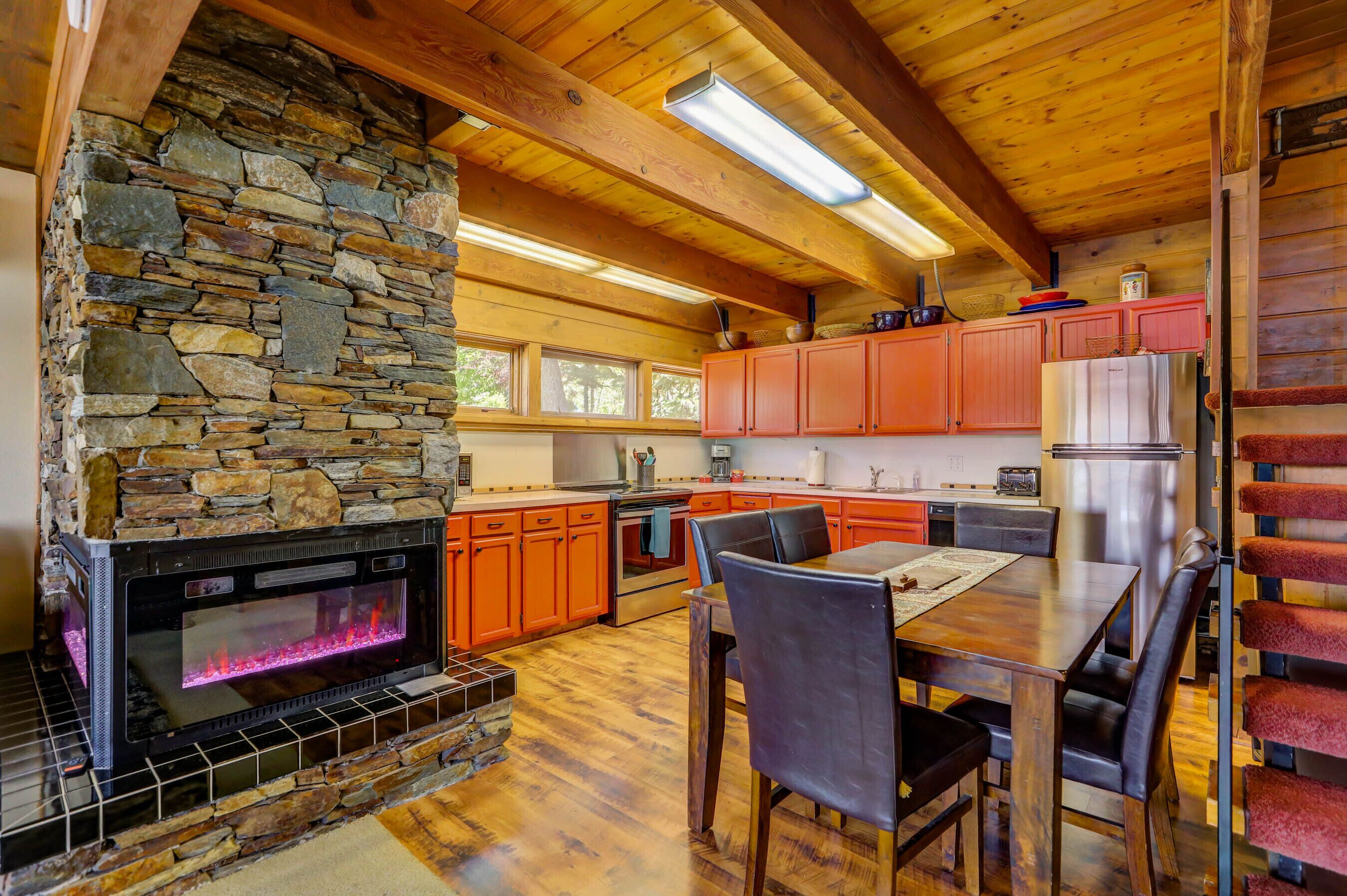 A rustic kitchen with a stone fireplace, wooden beams, and a dining area with a table and chairs.