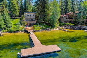 A lakeside property with a wooden dock leading to a house, surrounded by dense forest.