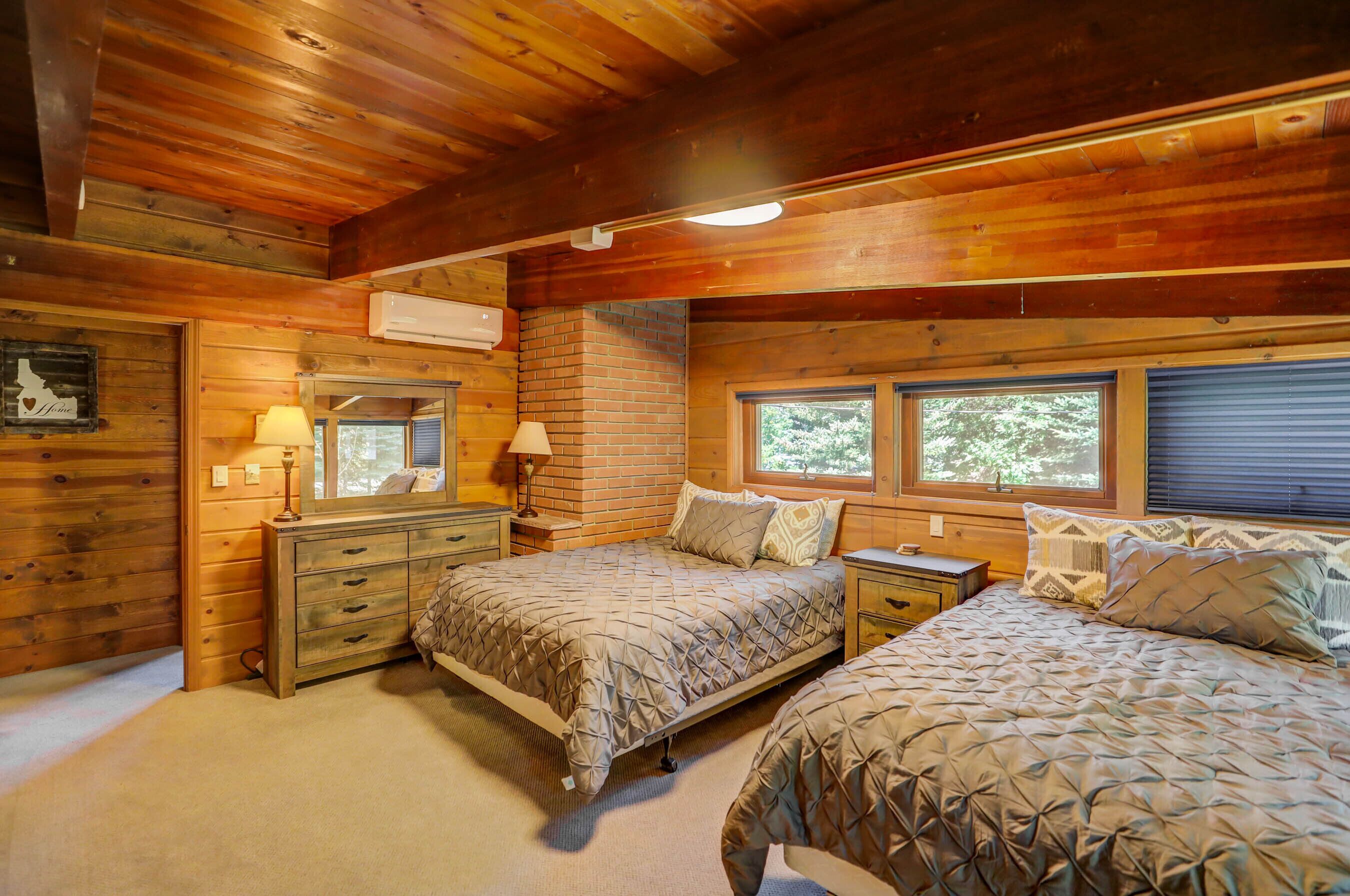 Une chambre dans une cabane en bois, avec deux lits, une commode et une fenêtre donnant sur la forêt.