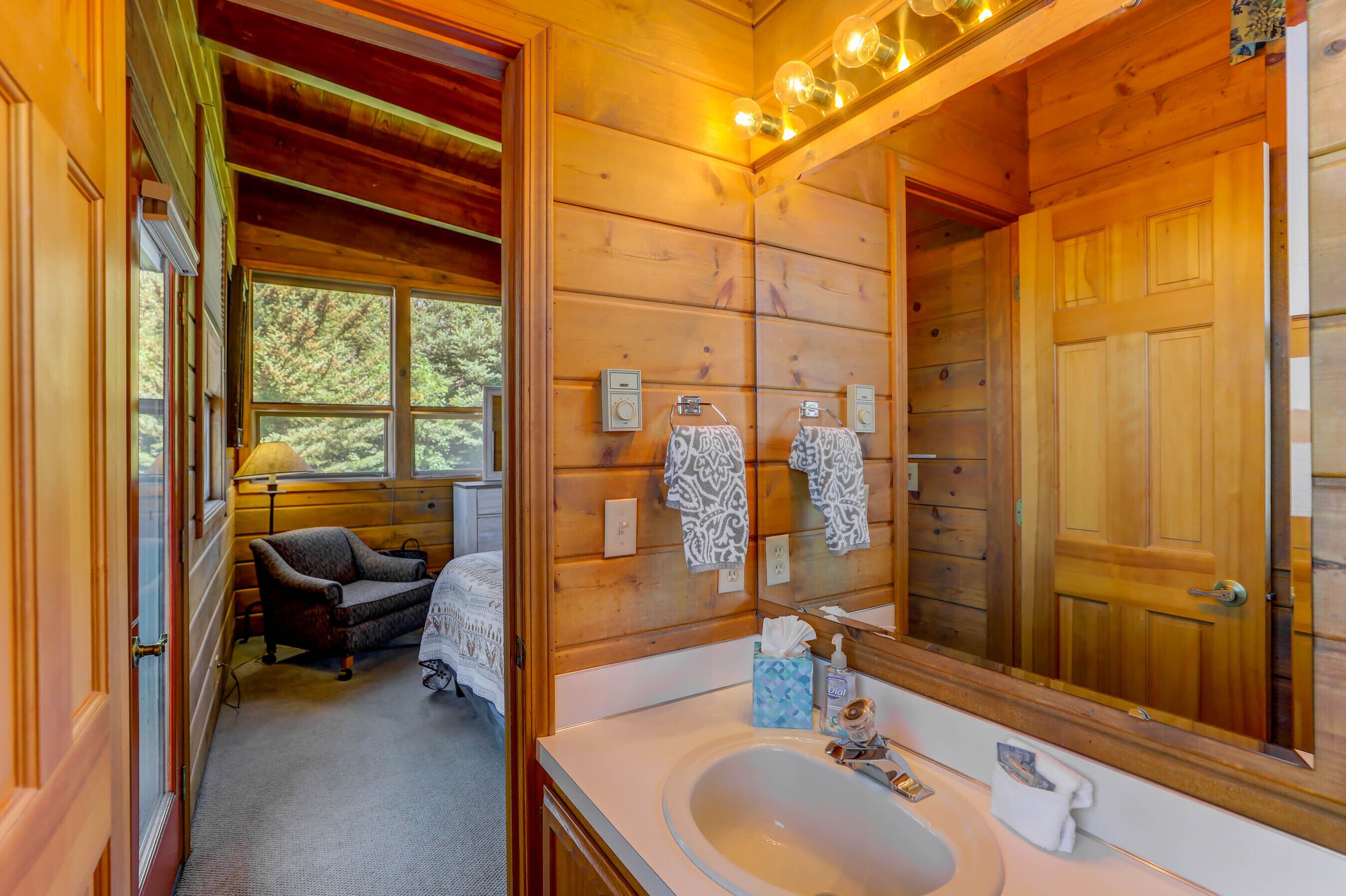A wooden cabin bathroom with a large mirror, a sink, and a chair.