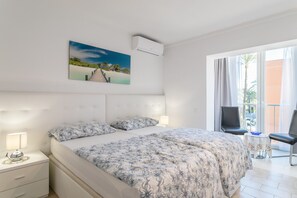 Une chambre à coucher avec un lit, des tables de chevet, une chaise, un balcon et un tableau au mur.