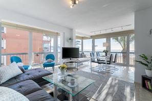 A modern living room with a glass coffee table, leather sofa, and a flat-screen TV.