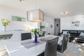 Una cucina moderna con mobili bianchi, un'area pranzo con tavolo e sedie bianche, e un divano in pelle nera nella zona living.