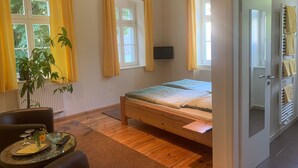 A bedroom with a bed, a TV, a potted plant, and a window with curtains. - Doppelzimmer 1 - Loensches Gut (Görlitz)