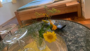 A room with a bed, a glass table with a vase of flowers, and a remote control. - Doppelzimmer 1 - Loensches Gut (Görlitz)