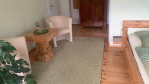 Ein gemütliches Zimmer mit Holztisch, weißem Stuhl, einer Zimmerpflanze und einem Bett mit gestreiftem Kopfkissen.