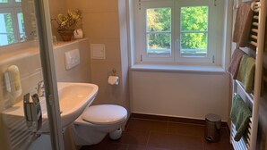 Ein Badezimmer mit Toilette, Waschbecken und einem Fenster mit Blick auf Bäume.