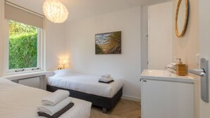 Ein Hotelzimmer mit zwei Betten, einem Fenster mit Blick auf Grünflächen, einem Bild an der Wand, einer Pendelleuchte und einem Waschbecken mit Holz-Seifenspender.