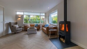 Ein modernes Wohnzimmer mit einem großen, schwarzen Kaminofen, zwei Sofas, einem Sessel und einem kleinen Tisch.