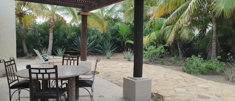 An outdoor patio with a round table and chairs, surrounded by palm trees and a pergola.
