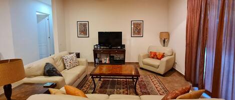 A living room with a sofa, armchair, coffee table, TV, and artwork on the walls.