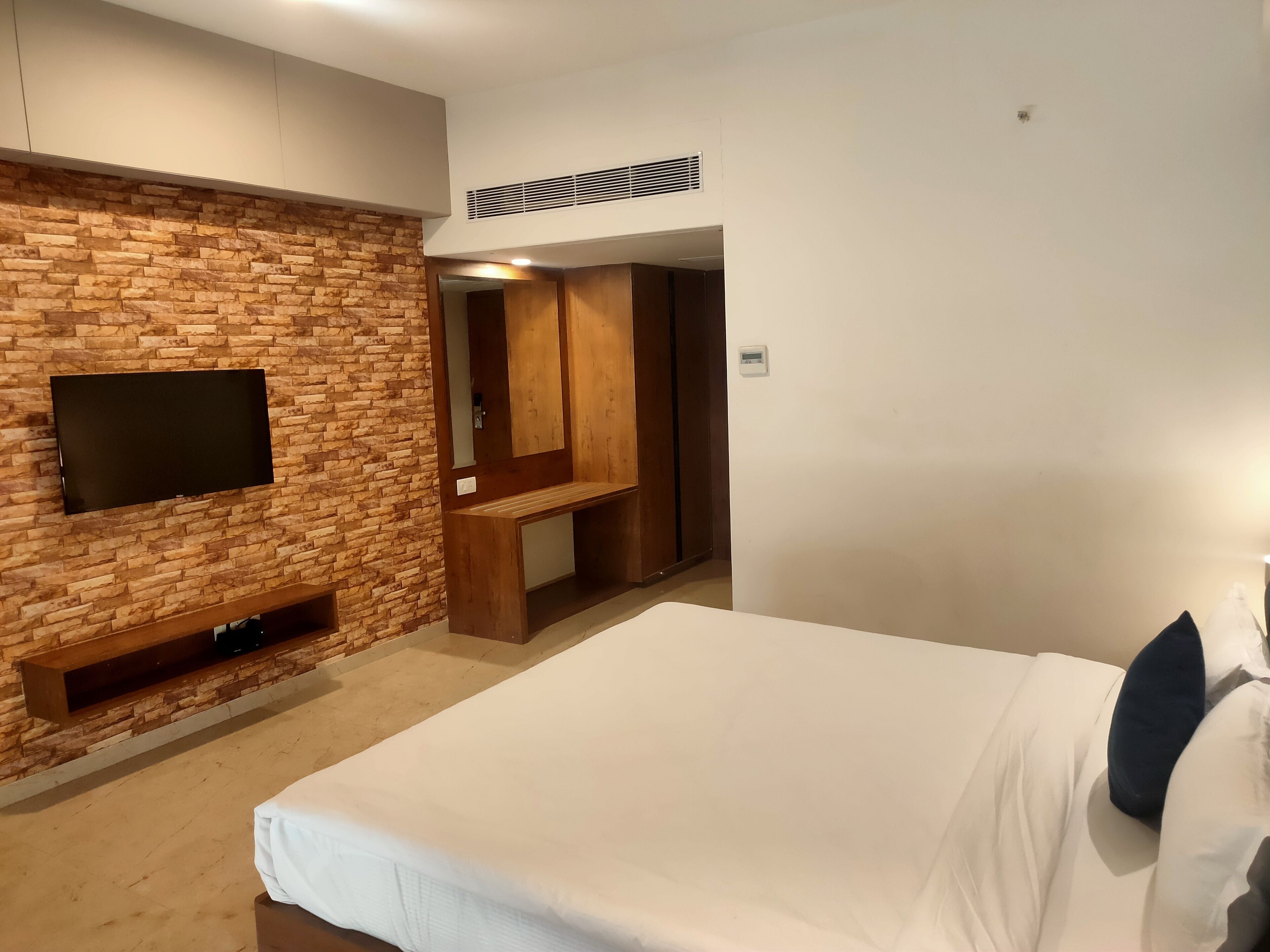 Habitación de hotel moderna con pared de ladrillo, televisor de pantalla plana, banca de madera y cama con almohadas.