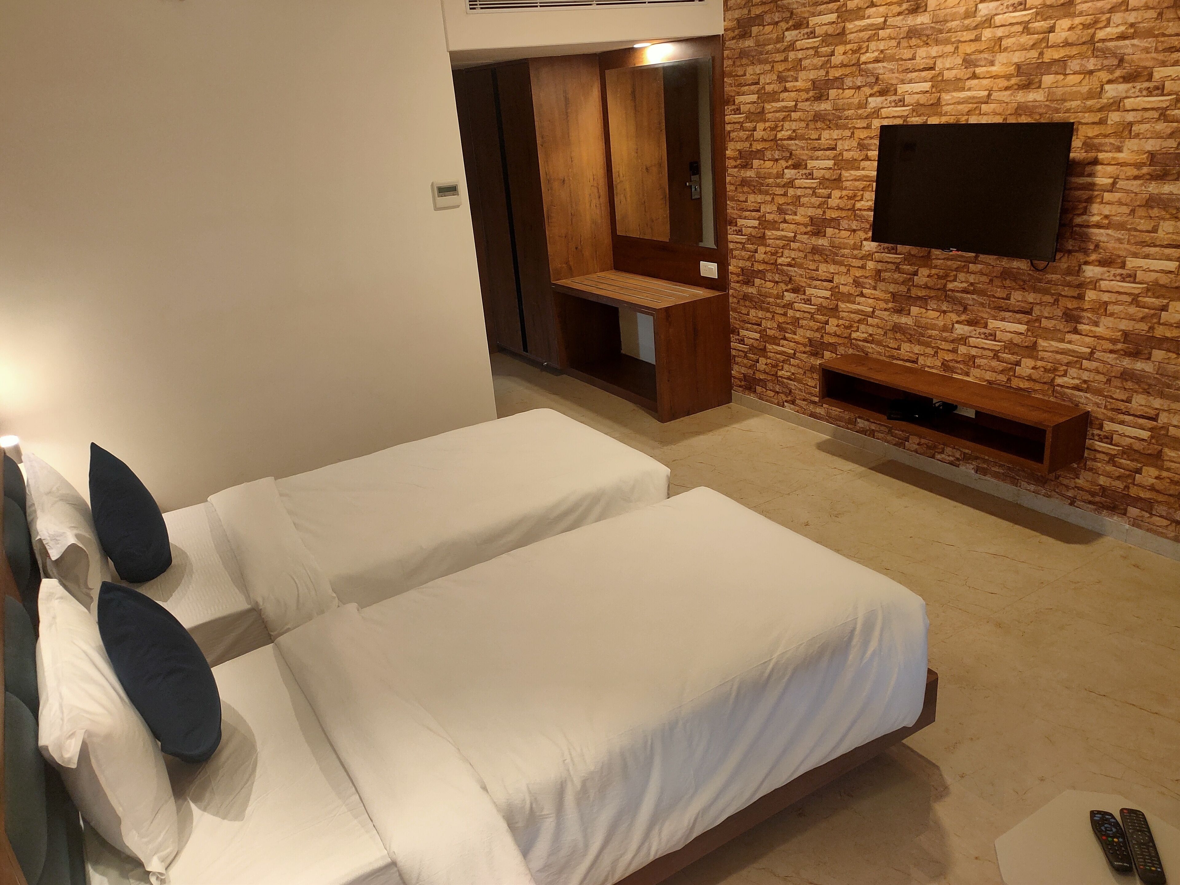 Una habitación de hotel con dos camas, un televisor montado en una pared de piedra, un armario de madera y un banco.