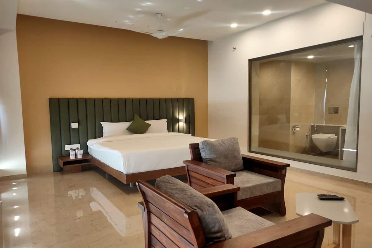 A modern hotel room with a large bed, wooden furniture, a glass shower enclosure, and a large mirror.