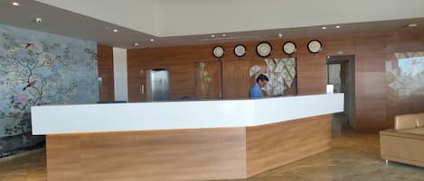 A modern reception desk with a wooden finish, a digital clock, and a mural of birds on the wall.