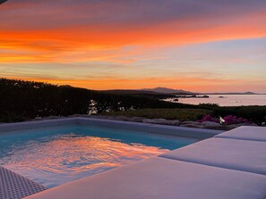 A swimming pool with a sunset view, surrounded by lounge chairs and a landscaped garden.