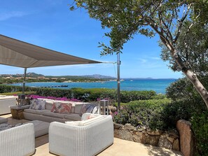 An outdoor seating area with a view of the sea, a covered patio, and a stone wall.