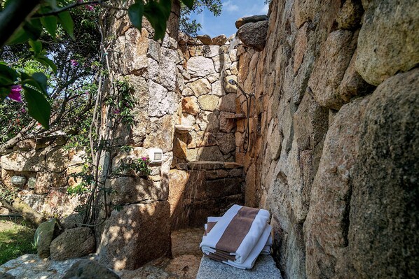 A stone-walled alcove with a towel, a small water feature, and greenery.