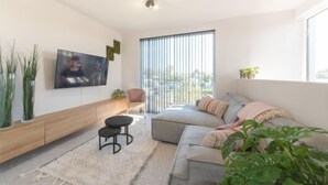 Una sala de estar moderna con un sofá, un televisor montado en la pared, una mesita y una ventana con persianas.