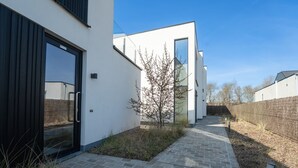 Un edificio moderno con un sendero pavimentado, un árbol pequeño y una pared de ladrillo.