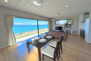 A modern kitchen with a dining area, large windows with a view of the sea, and a flat-screen TV. - Ocean View/ Rooftop sauna &BBQ/ 12 People/PADEL 2F (Uruma)