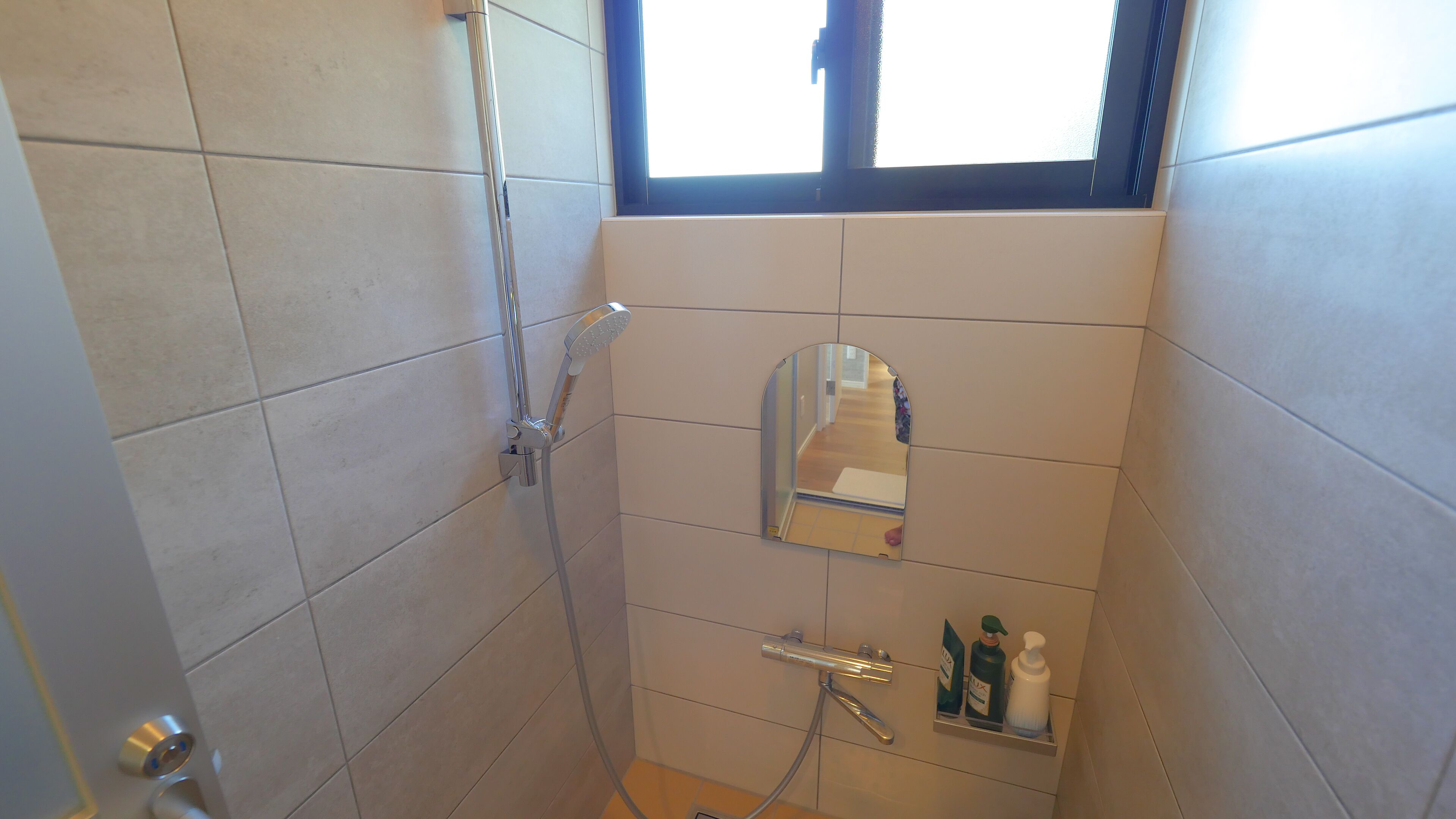 Een compacte badkamer met douche, spiegel en een plank met toiletartikelen.