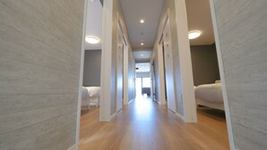 A narrow hallway with wooden flooring and white walls, leading to a bedroom with a bed and a nightstand. - Ocean View/ Rooftop sauna &BBQ/ 12 People/PADEL 2F (Uruma)