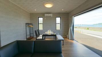 Uma sala de jantar moderna com uma mesa posta para dois, um sofá preto e vista para uma ponte e para a água.