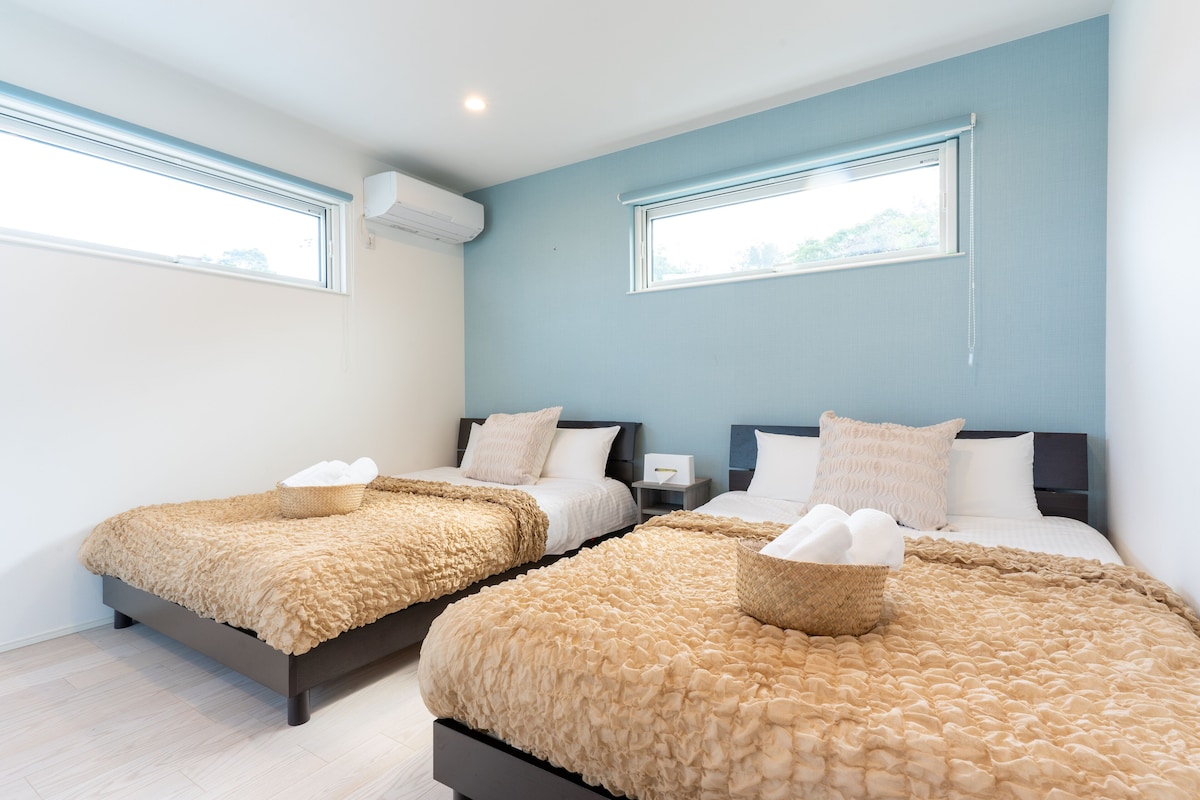 Une chambre d’hôtel avec deux lits, chacun recouvert d’une couverture beige à motifs et agrémenté d’un panier.