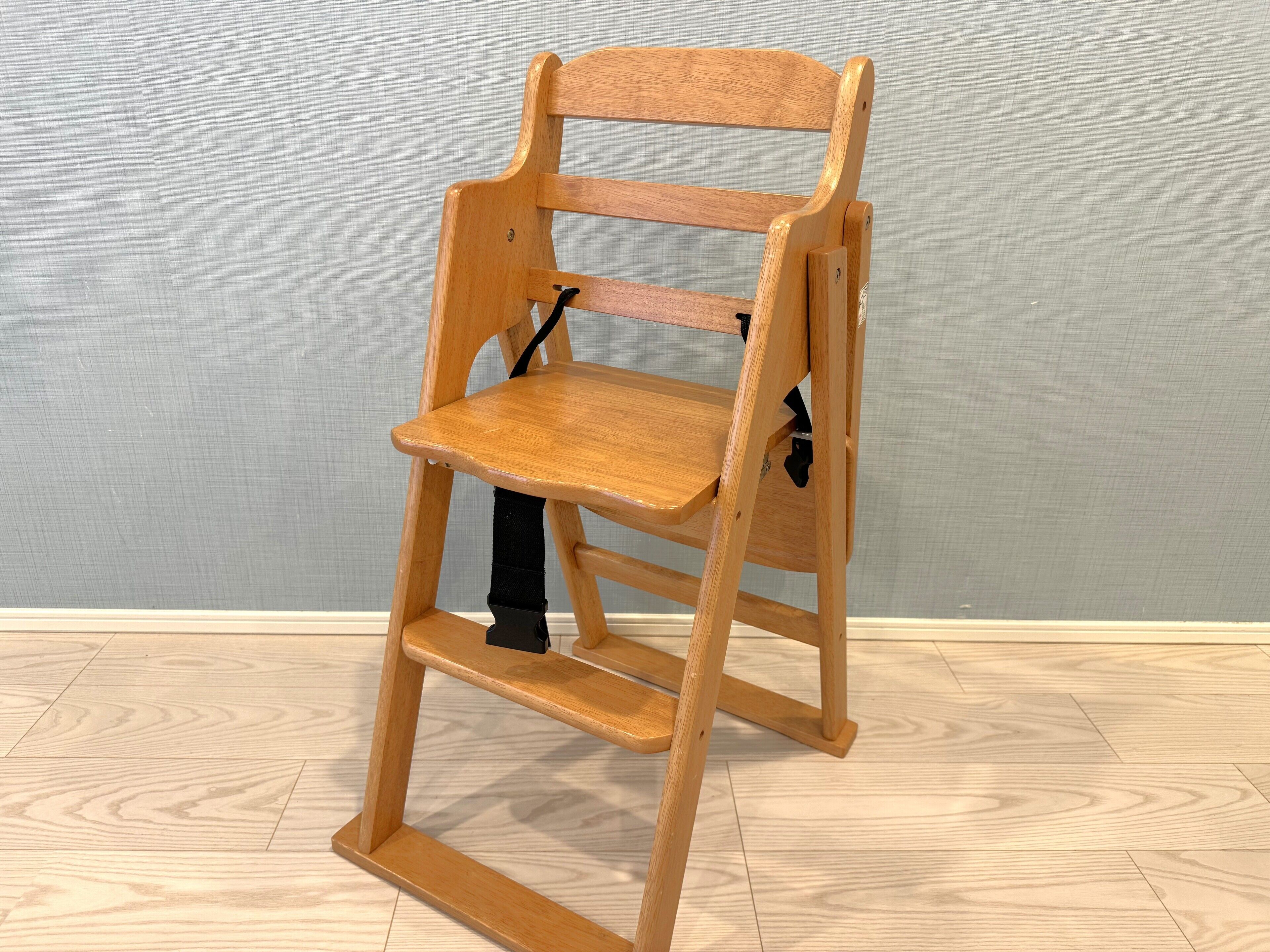 A wooden chair with a backrest, seat, and footrest, featuring a black strap for support.
