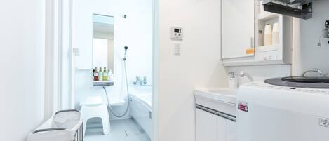 A modern bathroom with a glass shower enclosure, a white sink, and a built-in washing machine.