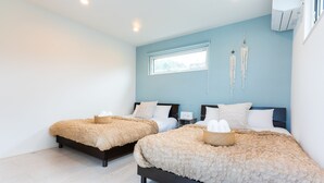 A bedroom with two beds, each with a ruffled blanket and a basket. There is a window with a view of trees, and an air conditioning unit on the wall.