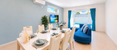 Un comedor moderno con una mesa dispuesta para cuatro personas, un sofá azul y un ventanal con cortinas.