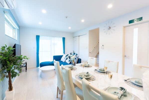 Un comedor moderno con una mesa de mármol, sillas blancas y un sofá azul al fondo.