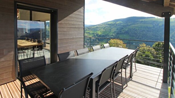Un espace repas extérieur moderne, doté d’une grande table et de chaises, offrant une vue imprenable sur un paysage magnifique.