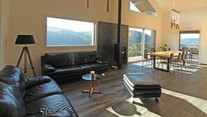 Un salon spacieux avec un canapé en cuir noir, une cheminée et un coin repas offrant une vue sur les montagnes.