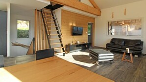 Un salon moderne avec un escalier en bois, un téléviseur à écran plat fixé au mur, un canapé en cuir noir et une table à manger en bois.