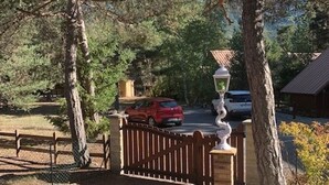 Un camino de entrada cerrado por una reja que lleva a un edificio con techo de metal, rodeado de árboles y una valla de madera.