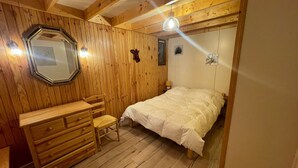 Un dormitorio con paneles de madera, una cama, cómoda, silla y espejo.