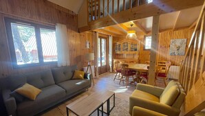 Un interior de cabaña acogedor con un sofá, sillones, una mesa de comedor y una zona de cocina.