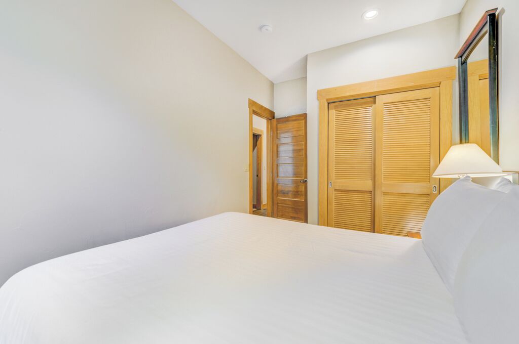 Una camera d'albergo con un letto, un armadio in legno e un comodino con una lampada.