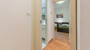 Un pasillo que conduce a un dormitorio con una cama, una mesita de noche y un cuadro en la pared.