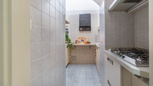 Una cocina estrecha con estufa a gas, una pizarra con la palabra 'Welcome' escrita y una pequeña encimera con un frutero.