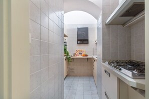 A narrow kitchen with a gas stove, a chalkboard with 'Welcome' written on it, and a small countertop with a fruit bowl. - GuestHost - Bologna Giardini Margherita Apartment (Bologna)
